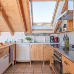 Küche mit Holzbalkendecke, Dachfenster und Edelstahlspüle.