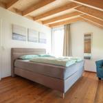 Schlafzimmer mit Bett, Sessel und Holzboden. An der Wand hängen drei Bilder.