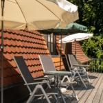 Terrasse mit Liegestühlen und Sonnenschirmen vor einem Haus mit Ziegeldach.