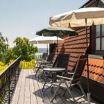 Terrasse mit Sonnenschirmen und Liegestühlen. Blick auf grüne Bäume und Wasser.
