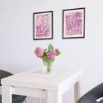 Weißer Tisch mit zwei schwarzen Stühlen und Blumen. Zwei Bilder an der Wand.