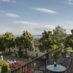Terrasse mit Tisch und Stühlen. Blick auf Straße, Bäume und Wasser.