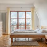 Schlafzimmer mit Holzbett, Fenster und Balkon. Parkettboden und Holzmöbel.