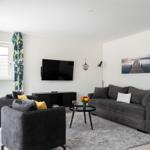 Wohnzimmer mit grauem Sofa, TV und Fenster mit floralen Vorhängen.