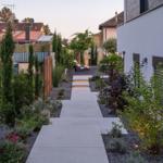Ein gepflasterter Weg führt durch einen modernen Garten mit Beleuchtung und Pflanzen.