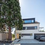 Moderne Villa mit Garage, großen Fenstern und einem hohen Baum vor dem Eingang.