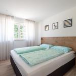 Schlafzimmer mit Doppelbett, Holzkopfteil, Fenster und Wandbildern.