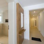 Flur mit Badezimmer und Holzgarderobe. Fliesenboden und schwarzes Teppichchen.