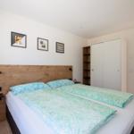 Schlafzimmer mit Doppelbett, Holzkopfteil und Wandbildern. Anschlussbad sichtbar.