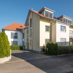 Modernes Mehrfamilienhaus mit Balkonen und begrünter Umgebung.