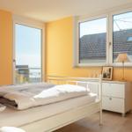 Schlafzimmer mit Bett, Schreibtisch und Fensterblick auf Dach