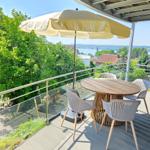 Terrasse mit Tisch, Stühlen und Sonnenschirm. Blick auf Grün und Wasser.