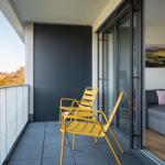 Terrasse mit zwei gelben Stühlen und Blick auf Wald und Hügel. Durchgehende Glastür zum Wohnzimmer.