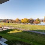 Blick von Balkon auf Grünfläche, See und Herbstbäume.