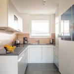 Moderne Küche mit weißen Schränken, dunkler Arbeitsplatte und Holzrückwand. Fenster und Küchenzeile sind sichtbar.