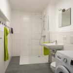 Badezimmer mit Dusche, Waschbecken und Waschmaschine.
