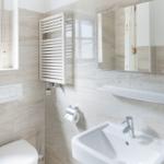 Badezimmer mit Toilette, Waschbecken und Spiegel an hellen Wandfliesen.