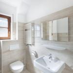 Badezimmer mit Toilette, Waschbecken und Spiegel. Holzfenster und Heizkörper.
