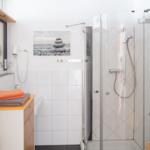 Bad mit Dusche, Waschbecken und Spiegel. Wandbild mit Steinen.