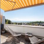 Terrasse mit Sonnenschutz, Liegestühlen und Blick auf See und Landschaft.