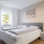 Schlafzimmer mit Doppelbett, Nachttisch und Fenster mit Blick auf Grünfläche.