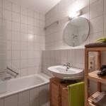 Bad mit Dusche, Waschbecken und Holzregal mit Handtüchern.