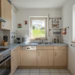 Küche mit Holzschränken, Spüle und Fensterblick auf Grünfläche.