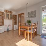 Esszimmer mit Holztisch, Stühlen und Balkonzugang. Hintergrund: Wohnbereich und Küche.