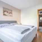 Schlafzimmer mit Doppelbett, Nachttisch und Bild an der Wand. Tür führt in die Badewanne.