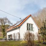 Ein weißes Haus mit rotem Dach und Solarpaneelen. Ein Balkon und ein Garagenbereich sind sichtbar.