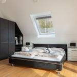 Schlafzimmer mit Dachfenster, Bett, Schrank und Nachttischen.