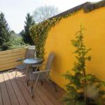 Terrasse mit Tisch und Stühlen, gelber Wand, Pflanzen und Blick auf Bäume.