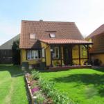 Ein gelbes Haus mit rotem Dach und Garten. Eine Terrasse mit Pflanzen.