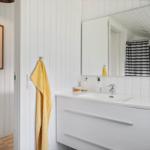 Badezimmer mit weißem Waschbecken, Spiegel und gelbem Handtuch an der Wand.