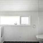 Badezimmer mit weißer Holzverkleidung, Fenster und schwarz-weißem Duschvorhang.