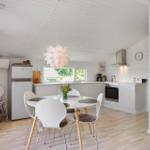 Küche mit Esstisch, Kühlschrank und Fenster. Weiße Wände und Holzboden.