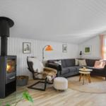Wohnzimmer mit Kamin, Sofa und Sessel. Holzboden und große Fenster.