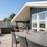 Terrasse mit Tisch, Stühlen und Flasche. Blick auf Haus und Grünflächen.
