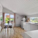 Küche mit Essbereich und Blick auf Garten. Holzboden, weiße Einrichtung und Fenster.