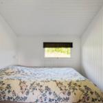 Schlafzimmer mit Bett und Fenster. Wände und Decke sind weiß verkleidet.
