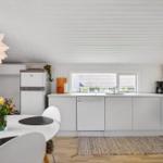 Küche mit Essbereich, weißer Einbauküche, Spüle und Fenster. Holzboden und Decke.