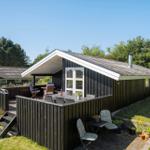 Schwarzer Holzhaus mit Terrasse und Garten. Gartenmöbel und Pflanzen sind sichtbar.