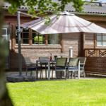Terrasse mit Tisch, Stühlen und Sonnenschirm vor Holzhaus mit Grasfläche.
