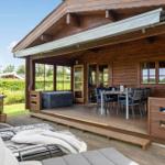 Terrasse mit Grill, Sitzgelegenheiten und Esstisch unter Markise. Holzhaus mit Fenstern und Türen.