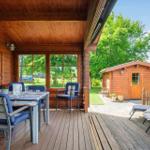 Terrasse mit Tisch und Stühlen, Holzhaus im Hintergrund, Garten mit Liegestühlen.