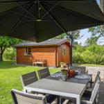 Terrasse mit Tisch, Stühlen und Sonnenschirm. Hinterhof mit Holzhaus und Spielplatz.