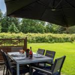 Terrasse mit Tisch, Stühlen und Sonnenschutz. Grünfläche und Hecke im Hintergrund.