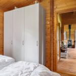 Schlafzimmer mit weißem Schrank und Blick in Wohnbereich mit Kaminofen.