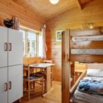 Schlafzimmer mit Doppelstockbett, Tisch und Schrank. Holzwände und -decke.
