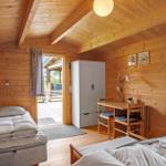Zimmer mit zwei Betten, Schreibtisch und Kleiderschrank. Holzwände und Decke. Tür zum Außenbereich.